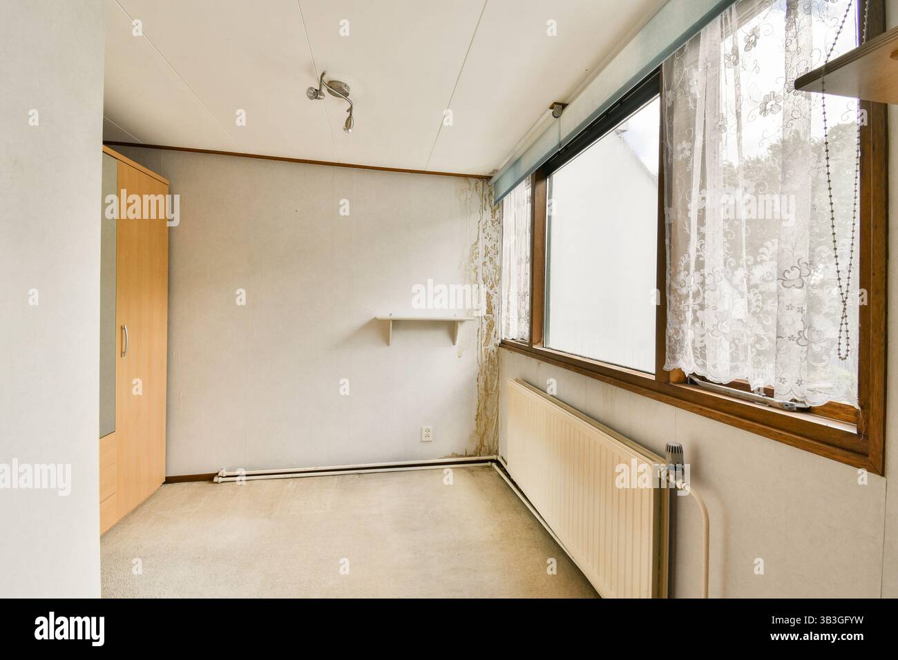 Ein heller und minimalistischer Raum mit großen Fenstern, die natürliches Licht ermöglichen, einem einfachen Schrank und neutralen Wänden, die eine klare Ästhetik bieten. Stockfoto