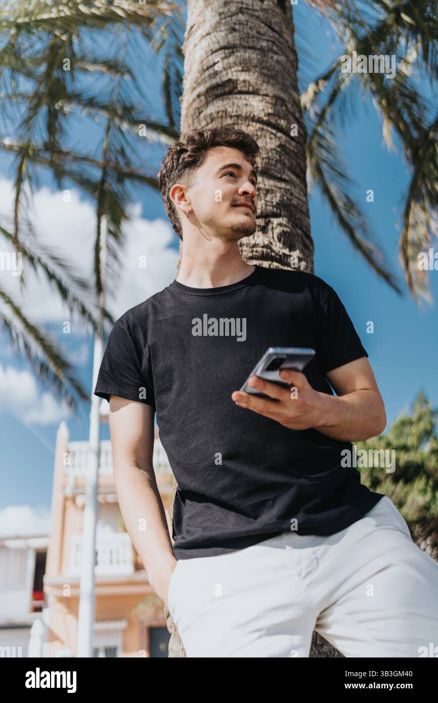 Junger Mann, der draußen ein Smartphone unter Palmen hält Stockfoto
