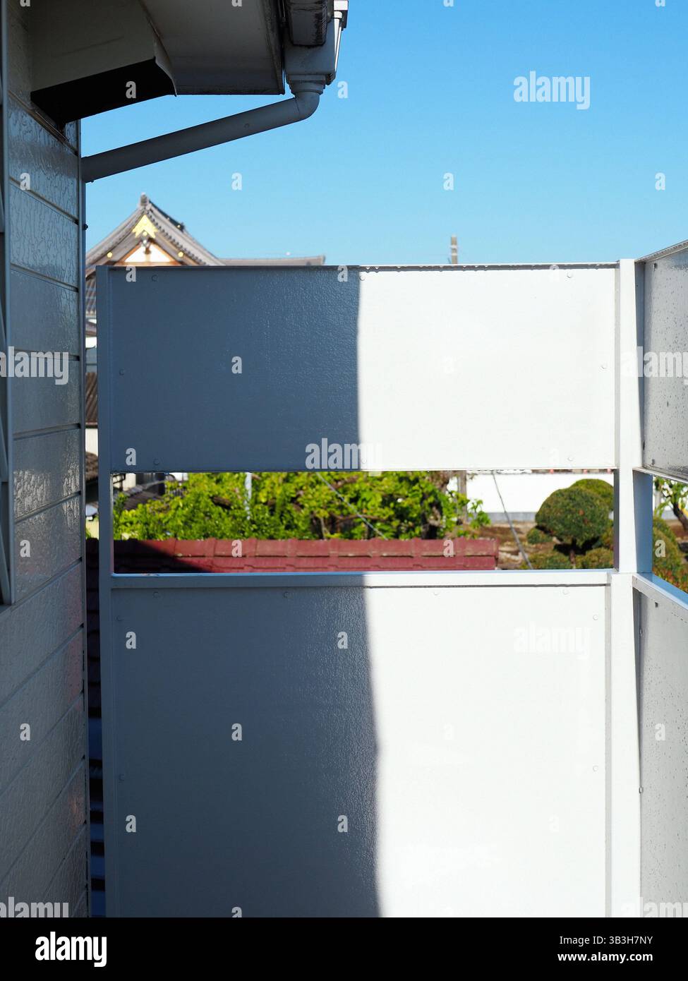 Morgenlicht wirft scharfe Schatten auf einen schmalen Balkon in einem japanischen Apartment Stockfoto