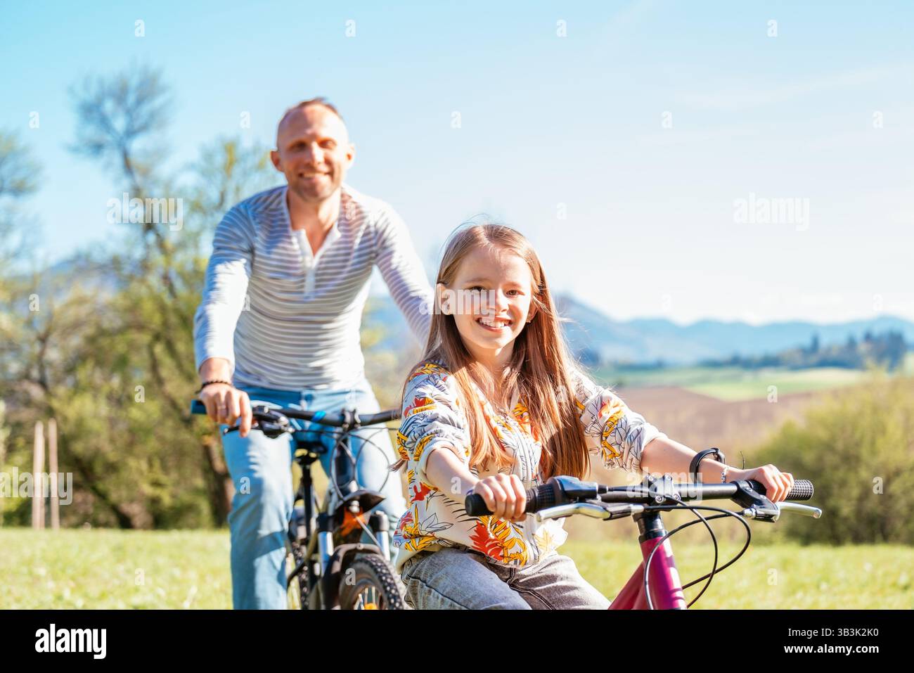 Porträt eines lächelnden Vaters mit seiner Tochter während einer Fahrradtour im Freien. Sie genießen eine gute gemeinsame Zeit in einem sonnigen Stadtpark. Glückliche Par Stockfoto