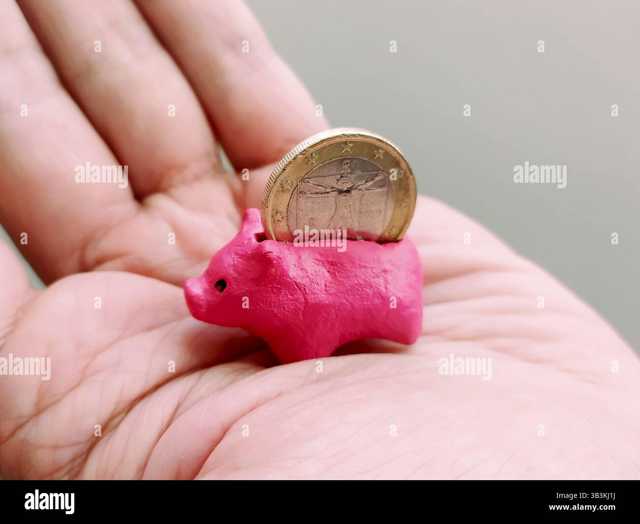 Winzige pinkfarbene Schweinebank auf einer Hand mit einer Münze. Metapher für Einsparungen, Investitionen, Finanzen und kleine Anfänge. Ideal für finanzielle Kompetenz oder Planung Stockfoto