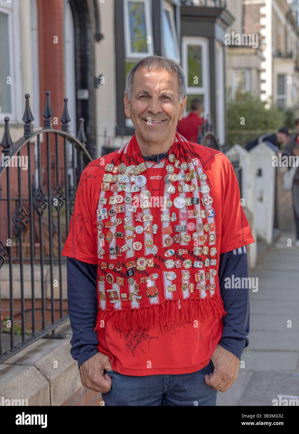 Männlicher Liverpool FC-Unterstützer mit Schal und vielen Abzeichen, die seine langjährige Liebe zum Verein zum Ausdruck bringen. Stockfoto