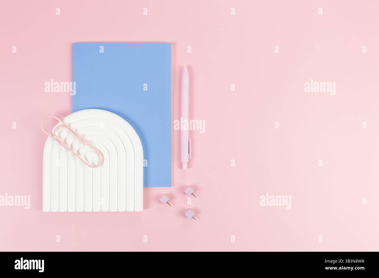 Ansicht von oben auf blaues Notizbuch, rosa Stift, Büroklammer, Stifte, weißes Bogenfach auf rosa Hintergrund. Schule, Bürotapete. Flache Ladefläche, Kopierraum. Stockfoto
