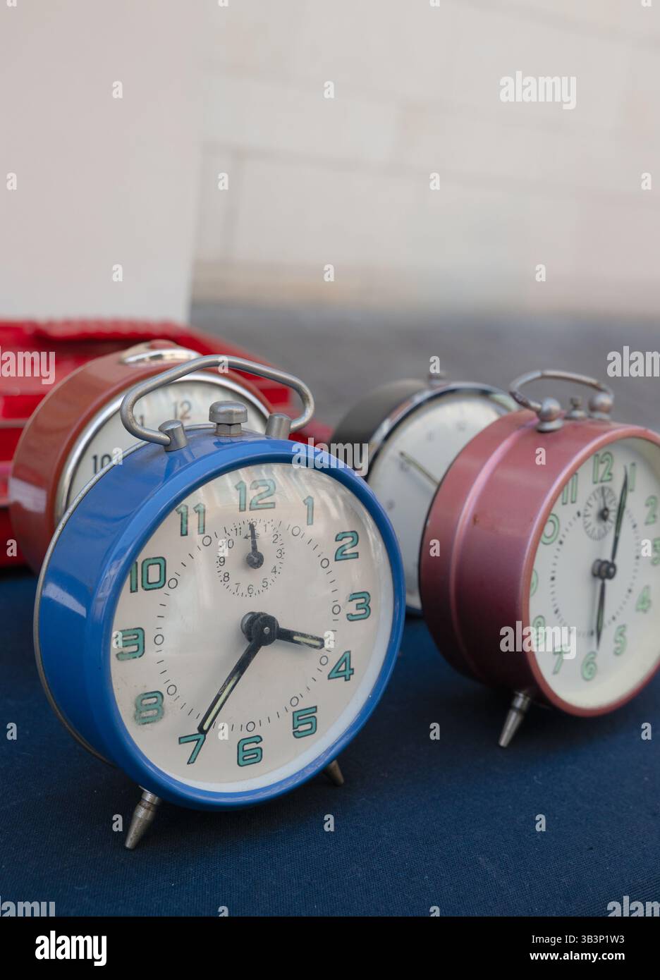 Eine bezaubernde Kollektion von Vintage-Weckern in verschiedenen Farben auf einer blauen Oberfläche, die den zeitlosen Charme von Retro-Design und Funktionalität zum Ausdruck bringt Stockfoto
