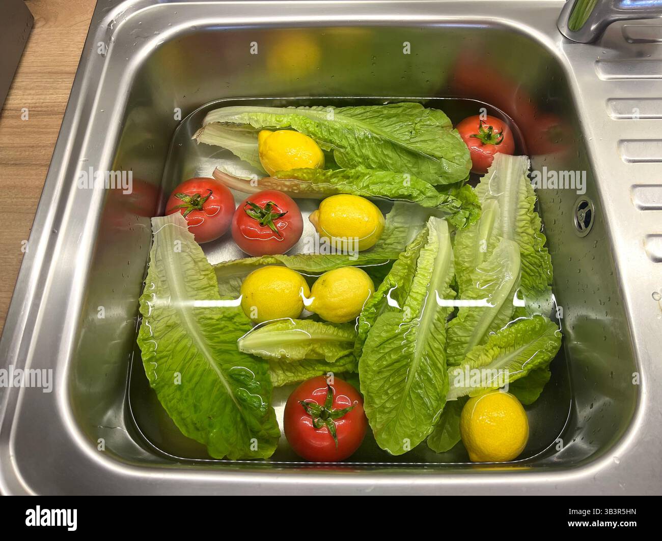 Zitronen, Tomaten und Salatblätter Spülen in einer Küchenspüle zu Hause, gesunde Mahlzeit Vorbereitung, Lebensmittelsicherheit, Lebensmittelhygiene, Hausmannskost, Gemüsebecken Stockfoto