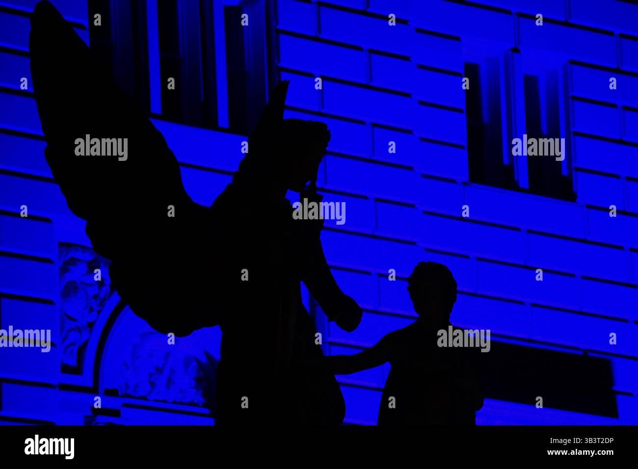 Dunkler Schatten einer klassischen Marmor-Engelskulptur mit mächtigen schwarzen Flügeln auf der Schlossbrücke, Berlin, vor tiefblauem Neonhintergrund bei Nacht Stockfoto