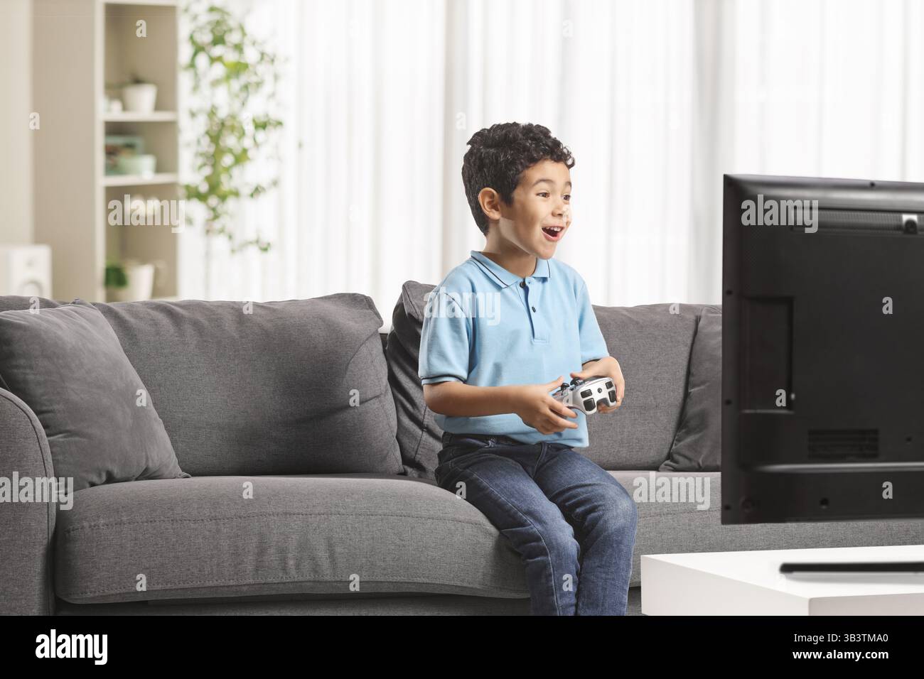 Ein aufgeregter asiatischer Junge sitzt auf einem Sofa und spielt Videospiele Stockfoto