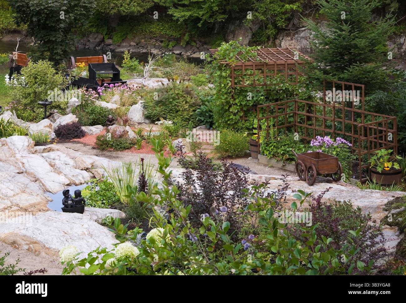 Pfad und Grenzen mit mehrjährigen Sträuchern, Pflanzen, Blumen einschließlich lila Phlox, Echinacea - Coneflower, Skulpturen, Ornamenten im Zen-Garten. Stockfoto