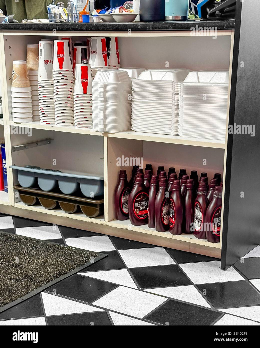 BAXTER, MN - 29. August 2024: Artikel, die hinter der Theke im Restaurant gelagert werden, darunter Getränketassen, Take-Home-Behälter und Schokoladensirup. Stockfoto