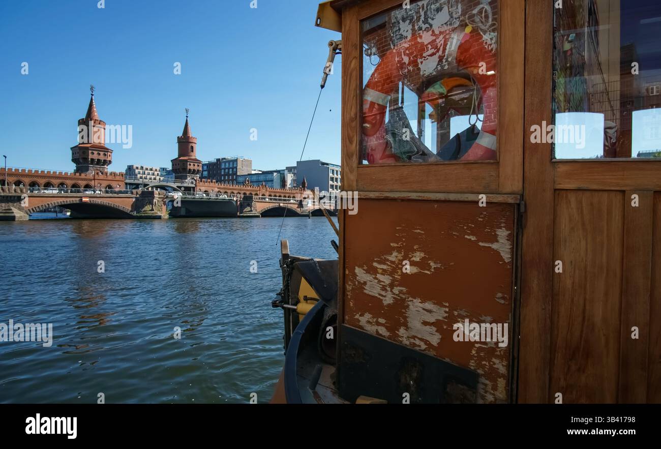Blick vorbei an einem rustikalen Holzboot auf der Spree in Richtung der historischen Oberbaumbrücke in Berlin an einem sonnigen Tag. Stockfoto