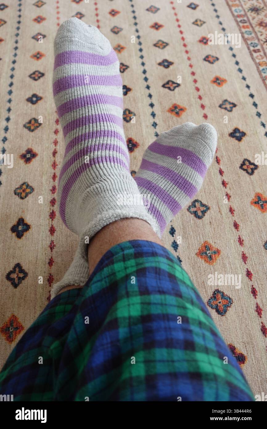 Gemütliche Füße in bunten Socken auf einem gemusterten Teppich zu Hause Stockfoto
