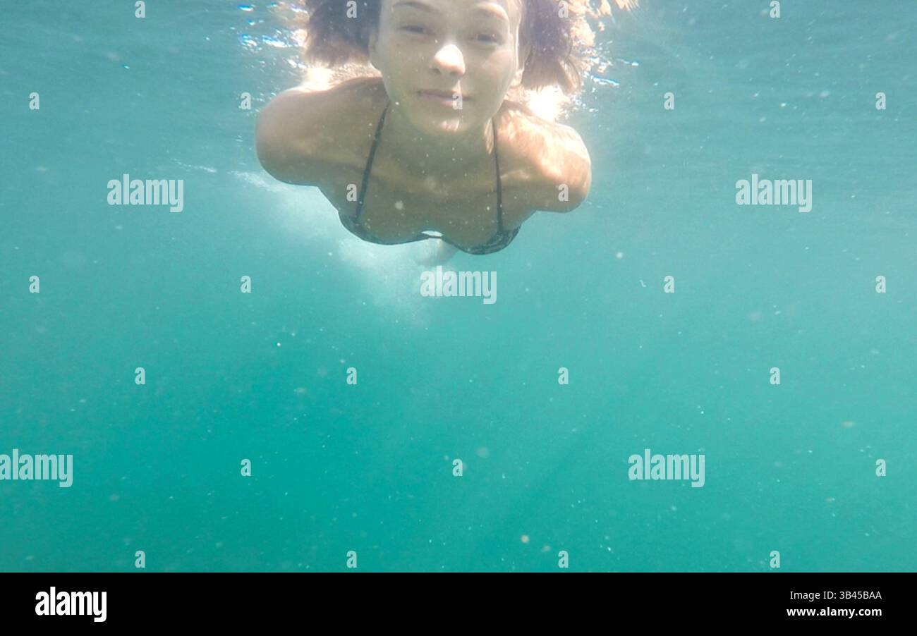 Die junge Frau schwimmt von der Oberfläche unter dem Wasser zur Kamera und schaut in die Lanze. Schöne Frau unter Wasser während des Reiseurlaubs. Stockfoto