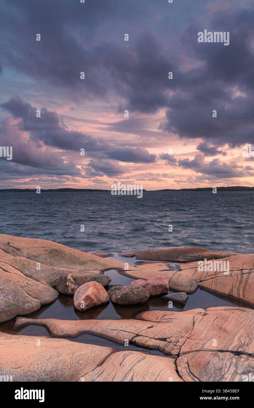 Die felsige Küste außerhalb von Göteborg bietet ruhiges Wasser, das den farbenfrohen Sonnenuntergang reflektiert. Wolken verleihen der ruhigen Atmosphäre Tiefe, perfekt für die Natur Stockfoto