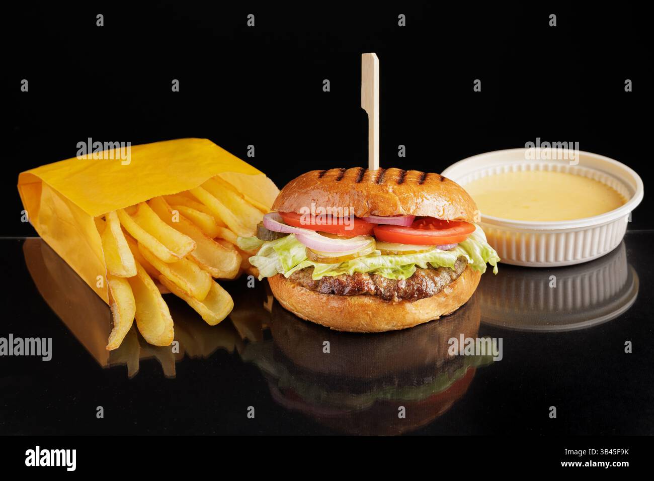 Köstlicher Cheeseburger mit frischen Pommes frites in gelbem Papierbeutel und Dipping-Sauce auf schwarzem reflektierenden Hintergrund. Stockfoto