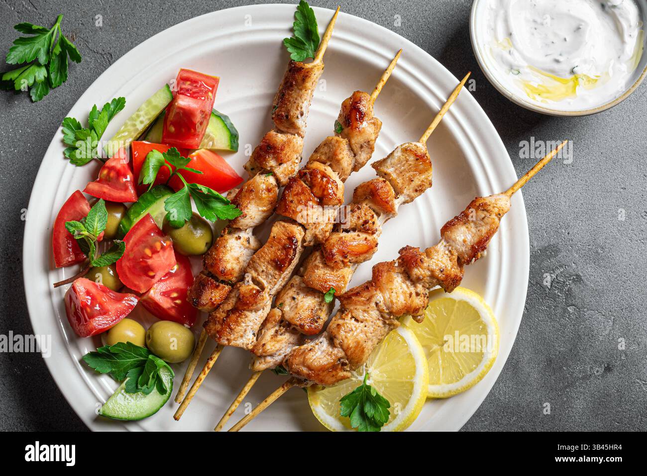 Gegrillte Hähnchenkebabs mit frischem Gemüsesalat auf Teller, Draufsicht, Kopierraum. Mediterranes Keto-Mittagessen mit gebratenen Fleischspießen, Tzatziki-Sauce A Stockfoto