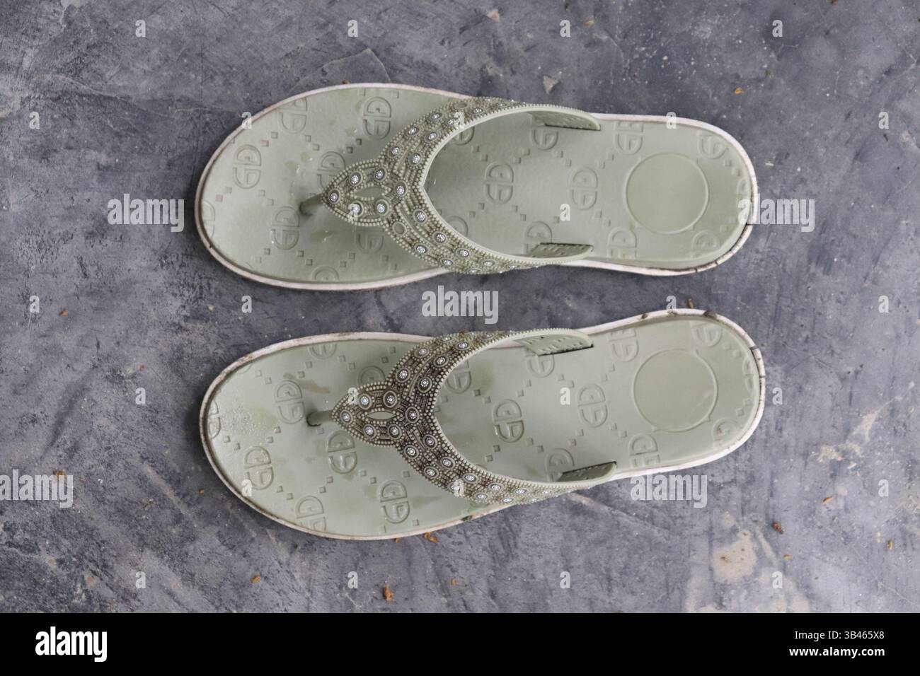 Overhead Shot zeigt zwei hellgrüne Sandalen mit Edelsteinverzierung auf einer grauen strukturierten Oberfläche, die Mode- und Sommerschuhe hervorheben. Stockfoto