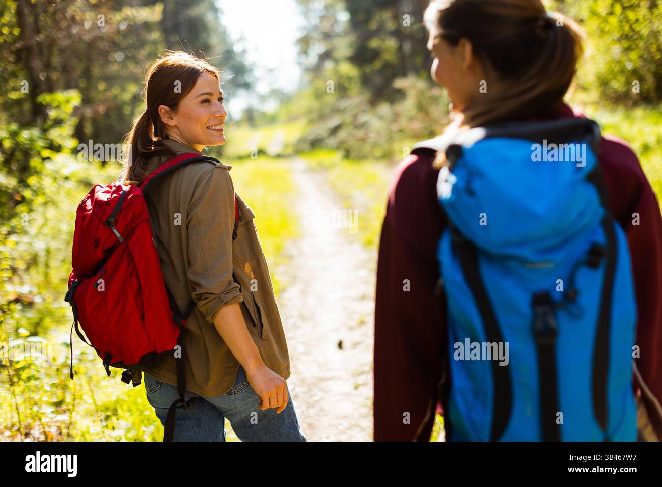 An einem hellen Tag wandern zwei Freunde gemeinsam auf einem üppigen Waldweg, voller Lachen und der Wärme der Freundschaft, umgeben von hohen Bäumen. Stockfoto
