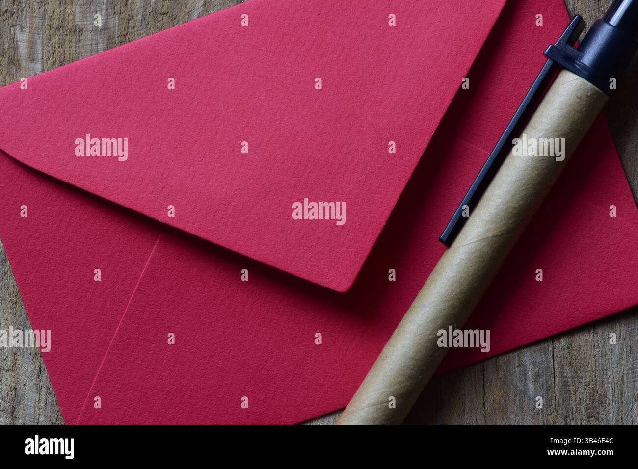 Kleiner roter Umschlag auf hölzernem Hintergrund und nachhaltiger Stift aus Recyclingpapier. Tageskarte für minimalistische Valentinstage. Stockfoto