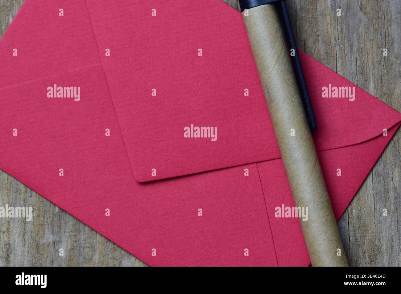 Kleiner roter Umschlag auf hölzernem Hintergrund und nachhaltiger Stift aus Recyclingpapier. Tageskarte für minimalistische Valentinstage. Stockfoto