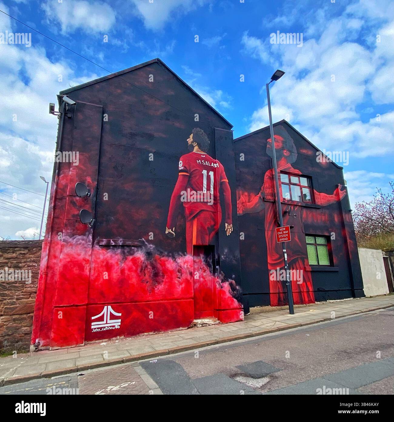 Mo Salah Wandgemälde des Künstlers John Culshaw an der Anfield Road, Liverpool, unter blauem Himmel und weißen Wolken. - Smartphone-aufgenommenes Stockfoto
