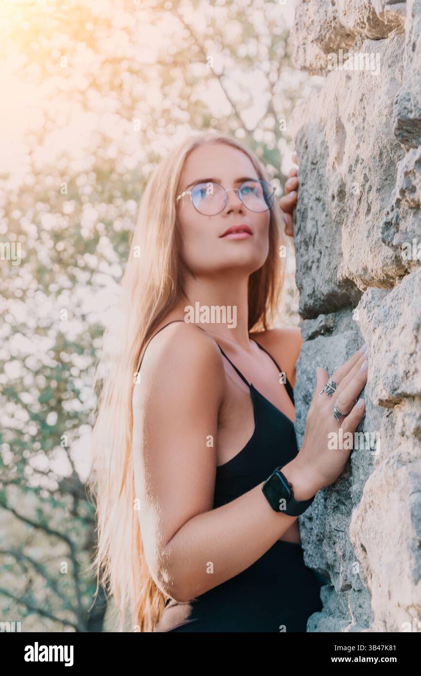 Frauenbrille Steinmauer - Porträt einer Frau mit Brille, die vor einer Steinmauer steht. Stockfoto