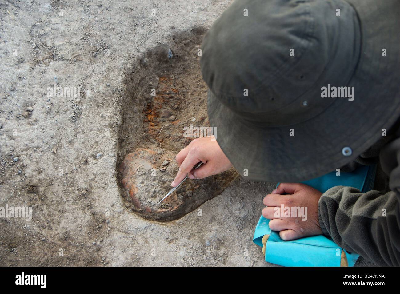 Archäologe gräbt sorgfältig verkohlte Sedimentschichten aus, um antike Artefakte und kulturelle Überreste in einer historischen Ausgrabungsstätte zu entdecken Stockfoto