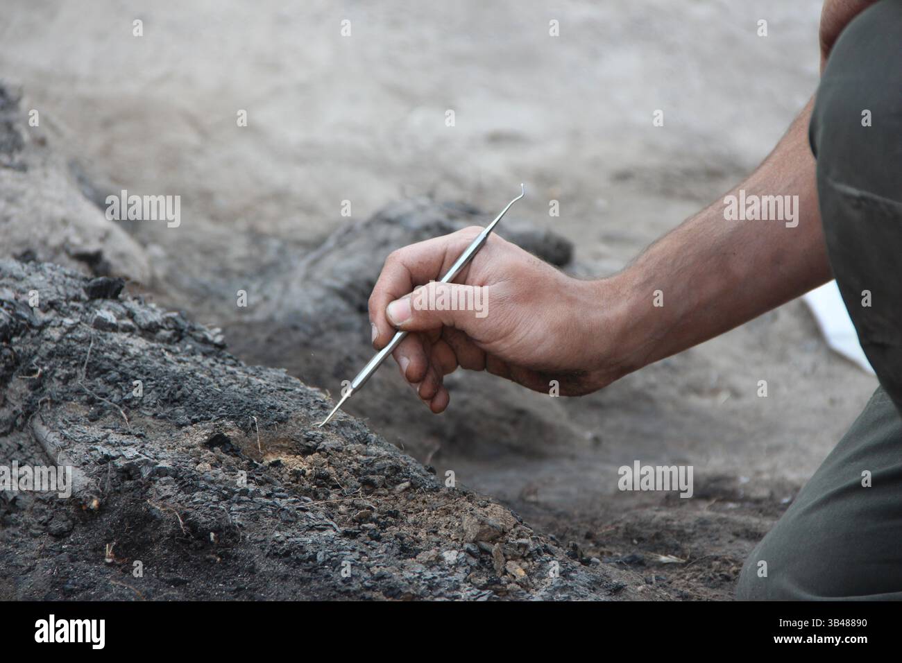 Archäologe gräbt sorgfältig verkohlte Sedimentschichten aus, um antike Artefakte und kulturelle Überreste in einer historischen Ausgrabungsstätte zu entdecken Stockfoto