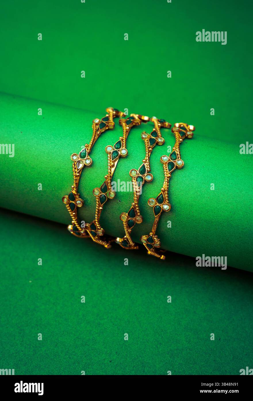 Handgefertigte goldene Armreifen mit komplizierten blattförmigen Designs auf einem kräftigen grünen Hintergrund, die traditionelle Eleganz und minimalistisch hervorheben Stockfoto