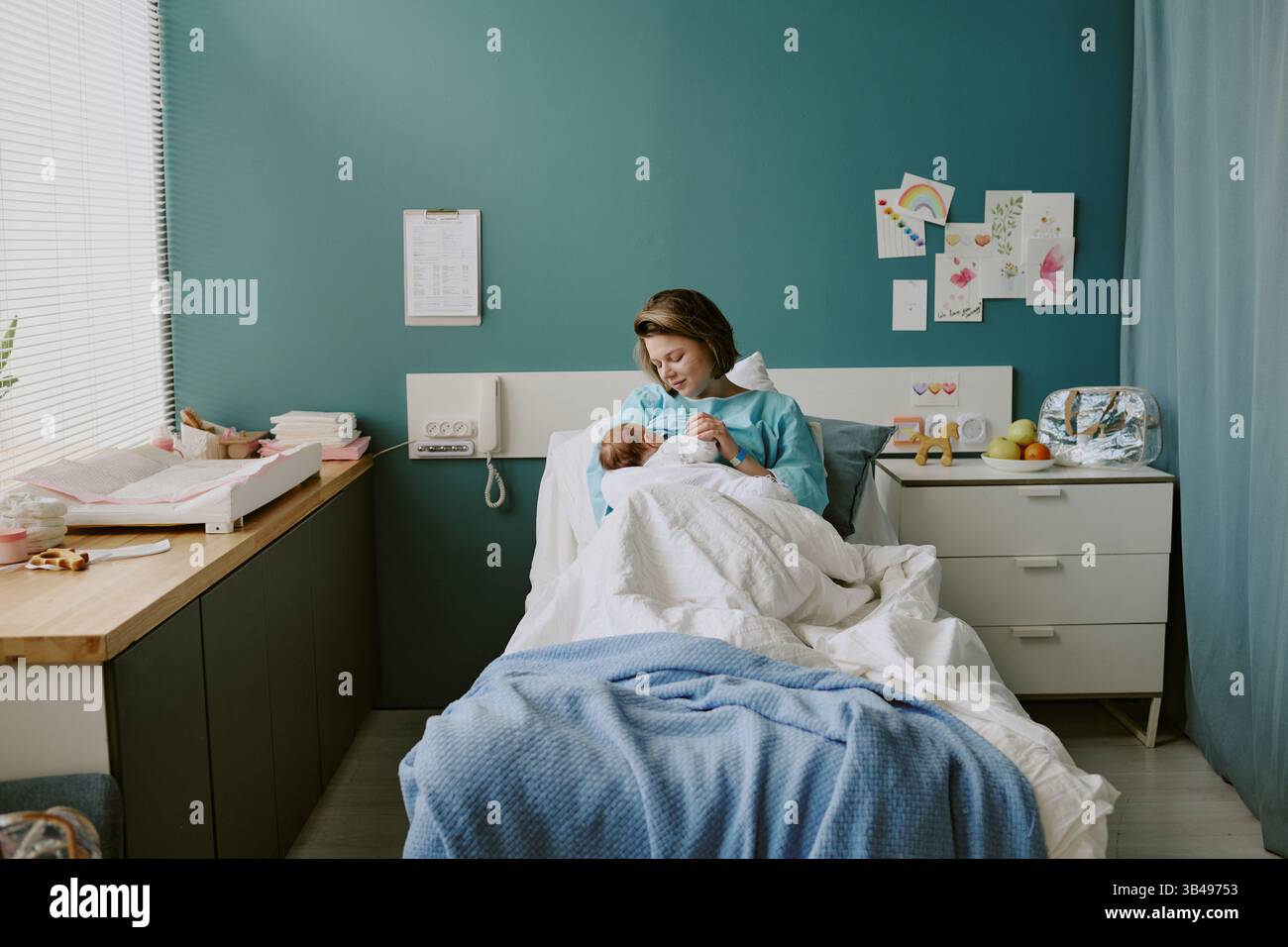 Krankenschwester hält Neugeborenes im Krankenhauszimmer gefüllt mit medizinischen Geräten und bunten Dekorationen an der Wand Stockfoto