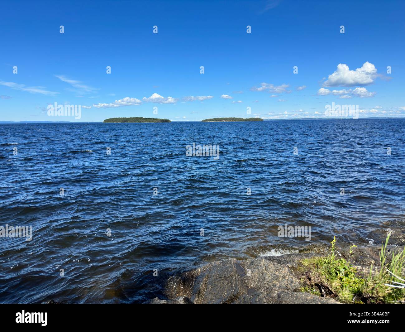 Der riesige See erstreckt sich unter einem klaren blauen Himmel mit ruhigen Inseln. Stockfoto