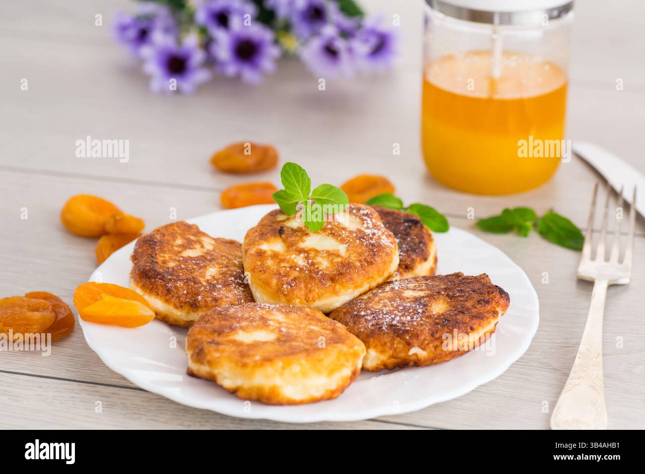 Ruddy-Käsepfannkuchen mit Honig und Minze auf einer weißen Platte. Stockfoto