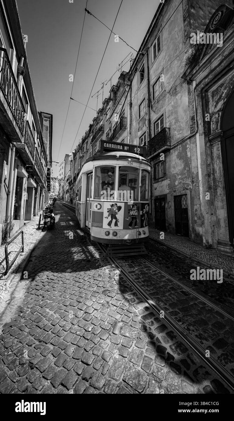 Historische Straßenbahn von Lissabon auf der Kopfsteinpflasterstraße in der Altstadt, Fotografie des alten portugiesischen öffentlichen Nahverkehrs in Schwarz-weiß-Optik Stockfoto