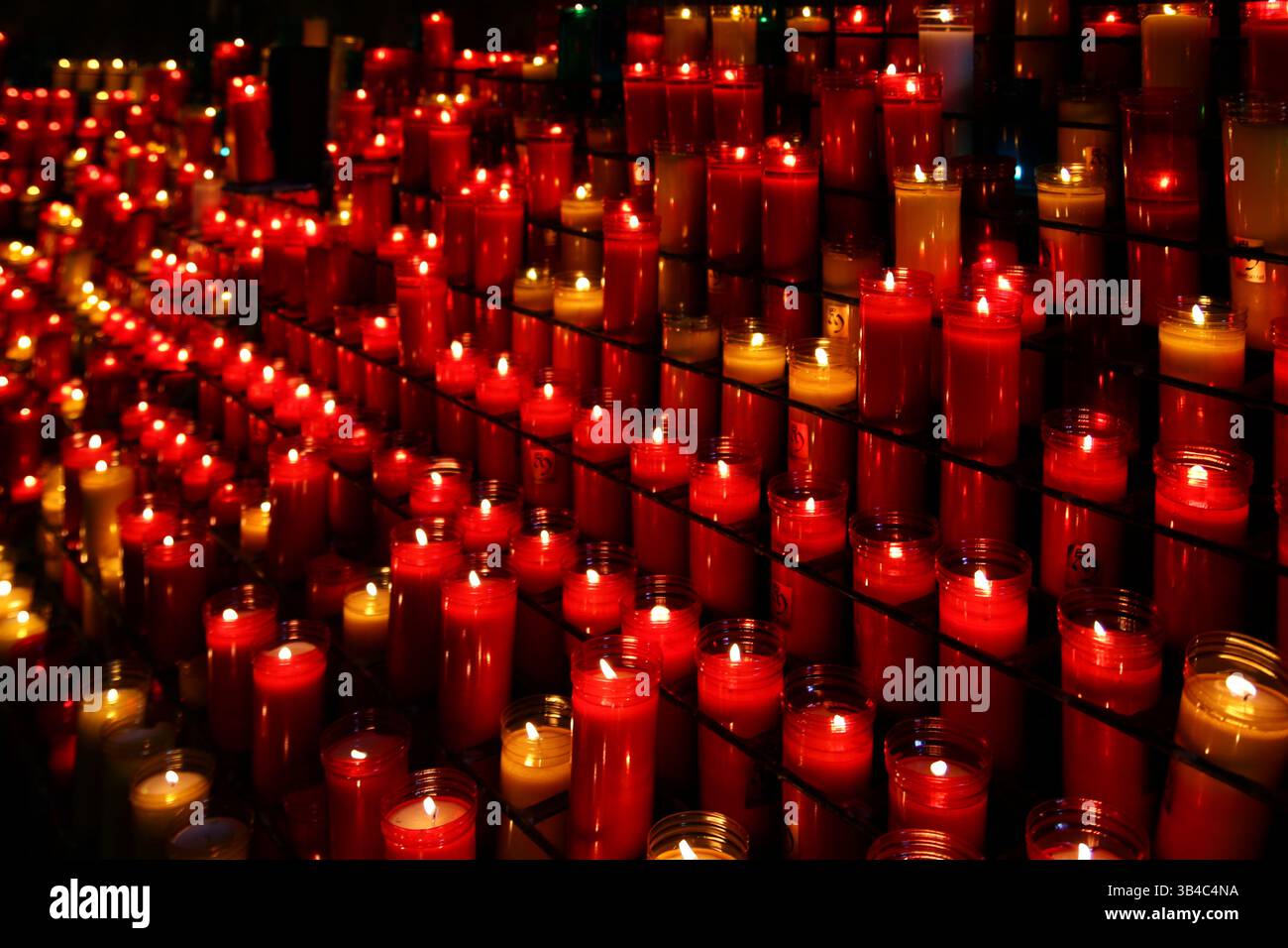 Dutzende glühender Votivkerzen, die in roten und weißen Glasbehältern brennen, symbolisieren Gebet, Erinnerung und spirituelle Hingabe. Stockfoto