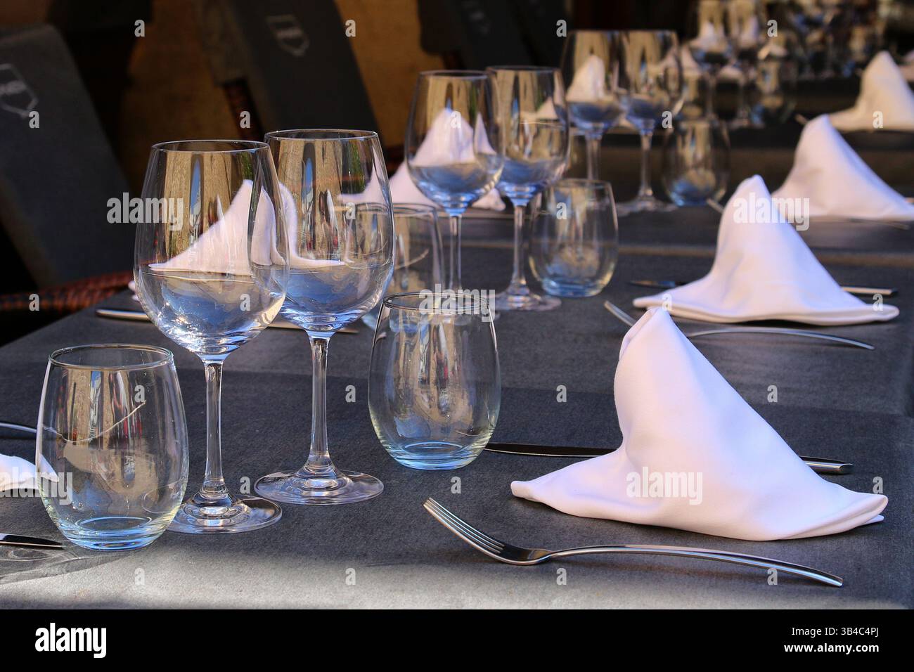 Nahaufnahme eines formellen Restauranttisches mit Weingläsern, Wassergläsern und gefalteten weißen Servietten auf einem dunklen Tuch, das an eine feine Atmosphäre beim Essen erinnert. Stockfoto