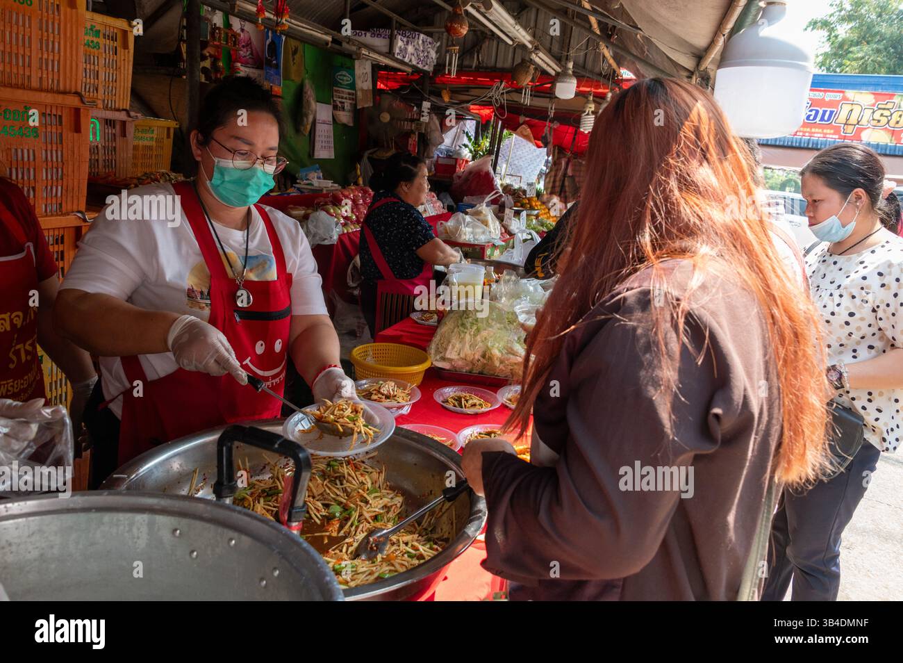 Eine Köchin bietet ihren Stammgästen an einem der Obststände kostenloses Mittagessen mit einer großen Auswahl an frischem Obst in der Muang Mai Marke an Stockfoto