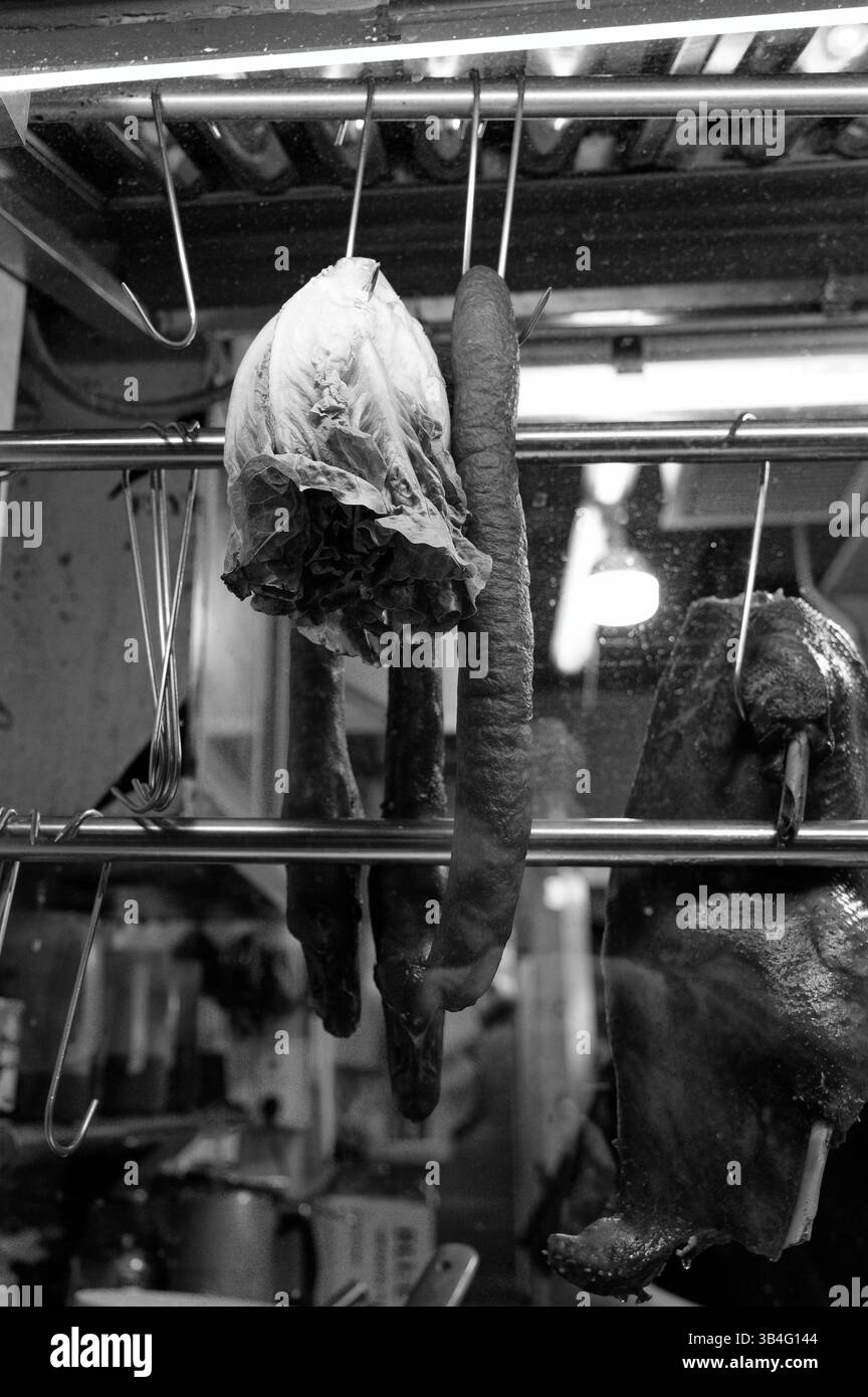 Schwarzweiß aus einer Marktküche: Salat, Wurst und Ente hängen nebeneinander Stockfoto
