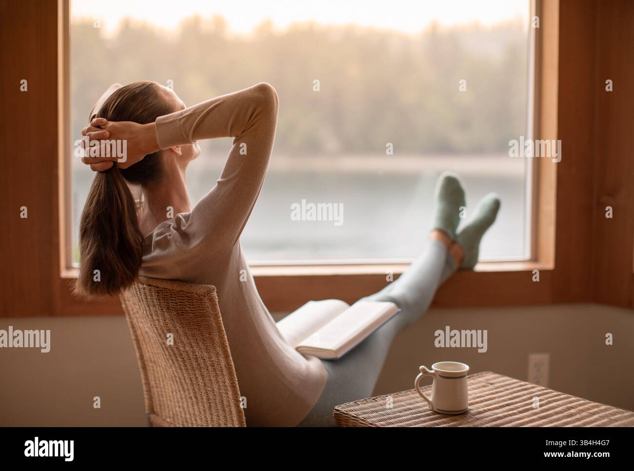 Person, die sich zu Hause beim Lesen eines Buches entspannt an einem gemütlichen Wintermorgen bei einer Tasse heißem Tee Kaffee fühlt Stockfoto
