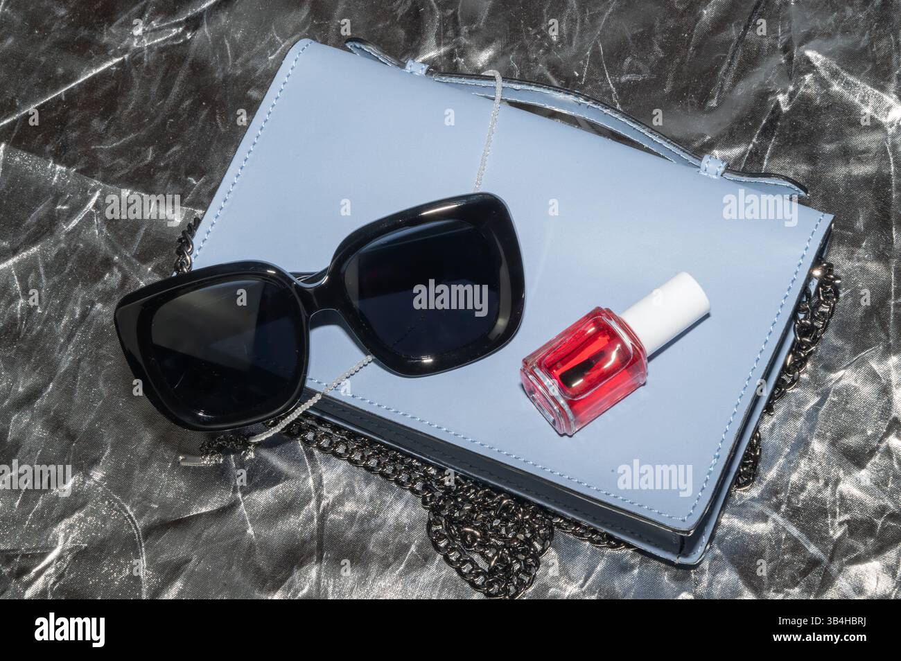 Eine stilvolle Sonnenbrille, eine modische blaue Handtasche und eine leuchtende Flasche roter nagellack sind unverzichtbare Accessoires für jedes Outfit Stockfoto