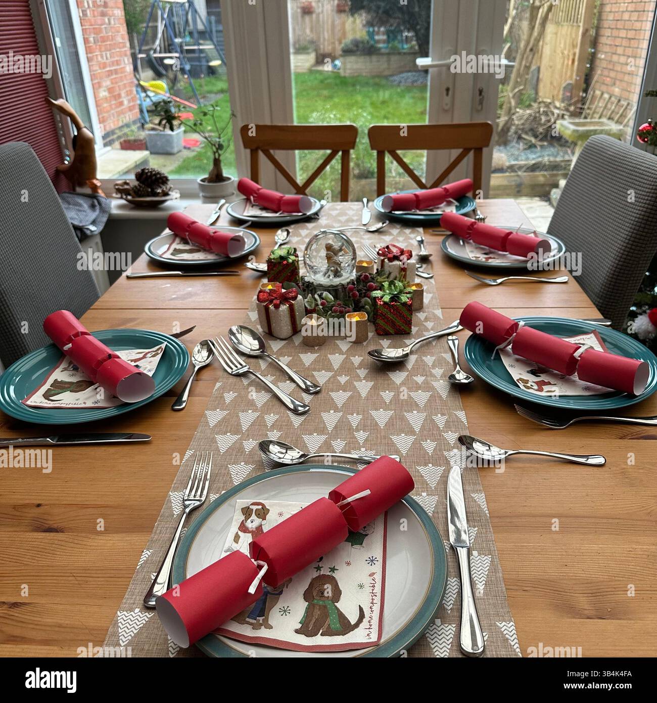Festliches Tischset zum Essen mit Schneekugel, Crackern, Tellern und Servietten in saisonalen Farben. - Smartphone-aufgenommenes Stockfoto