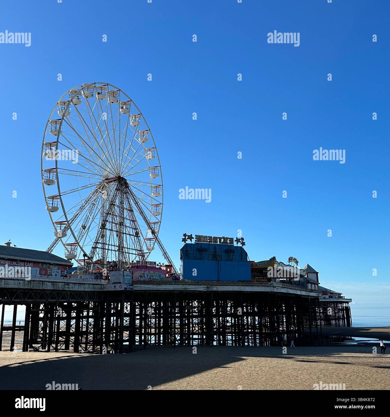 Blackpool Central Pier mit Riesenrad von der Promenade aus gesehen an einem sonnigen Tag mit blauem Himmel und Meer, Lancashire, England, Großbritannien. - Smartphone-aufgenommenes Stockfoto