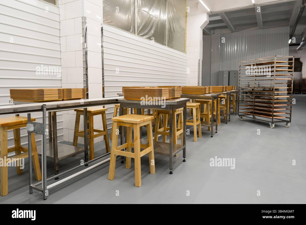 Sauberer Arbeitsbereich für die industrielle Lebensmittelproduktion mit Reihen von Edelstahltischen, Holzhockern und Tablettenstapeln Stockfoto