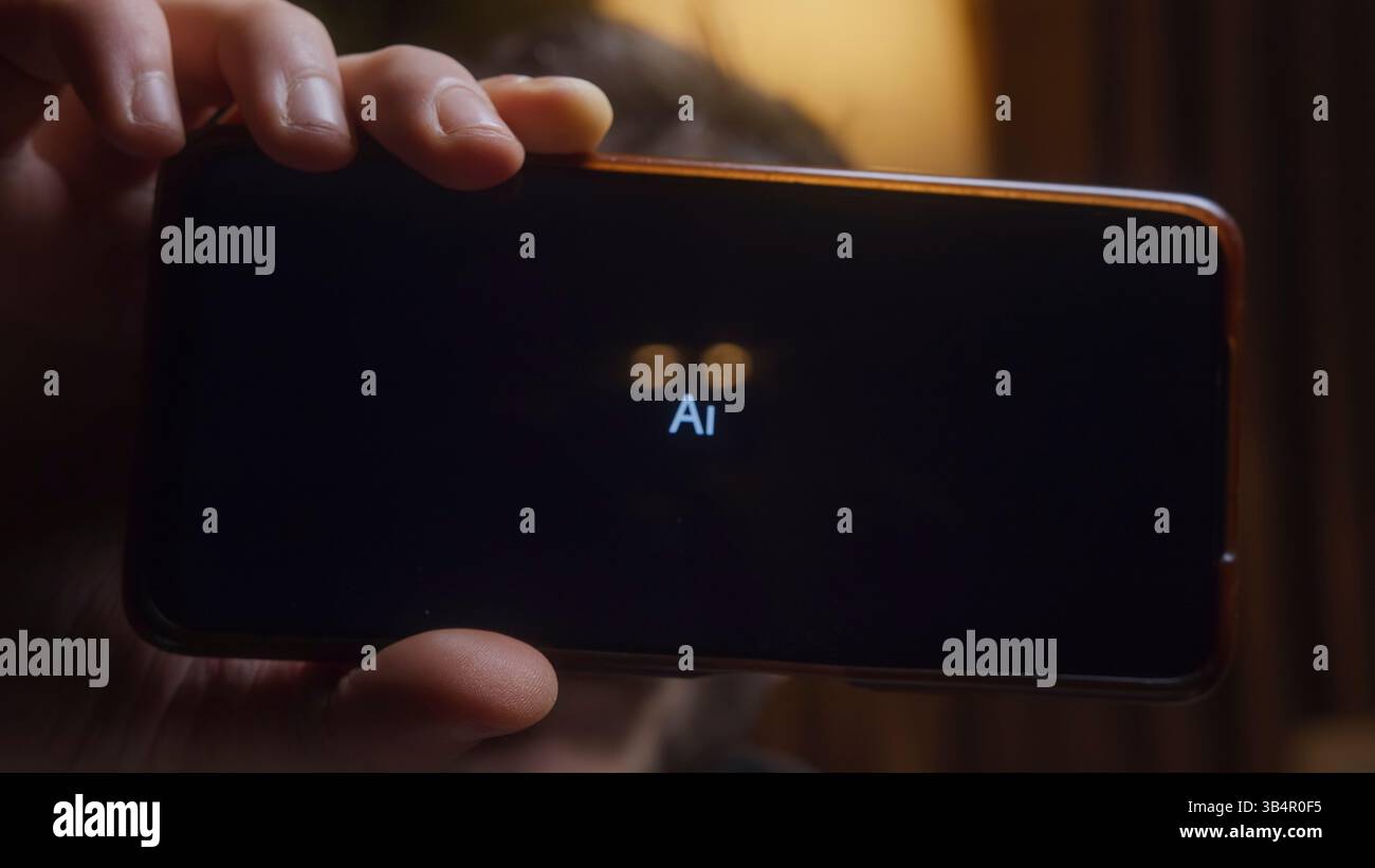 Nahaufnahme einer Hand, die ein Smartphone hält, mit einem dunklen Bildschirm mit einem leuchtenden KI-Ladesymbol, aufgenommen in einem schwach beleuchteten, gemütlichen Raum mit einem warmen Ambiente Stockfoto