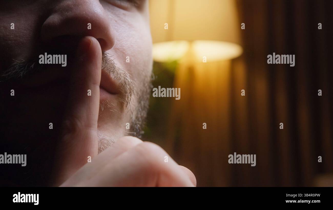 Nahaufnahme eines Mannes, der eine Stille Geste mit Finger auf den Lippen in einem schwach beleuchteten Raum macht Stockfoto