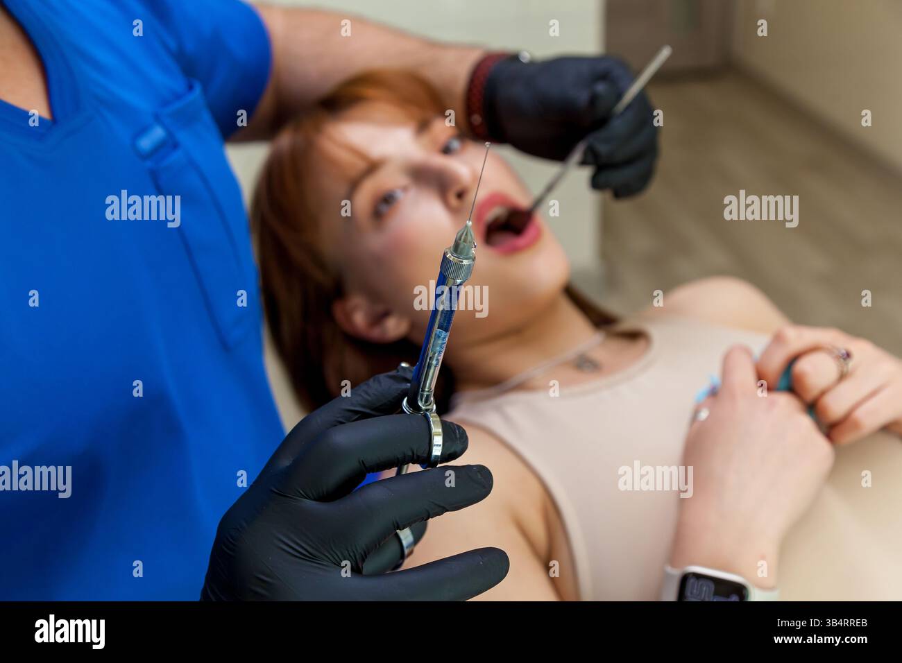 Nahaufnahme einer Zahnarzthandschuhhaltige Hand, die eine Spritze mit Narkosemittel hält, mit einer jungen Patientin, die im Hintergrund auf dem Zahnarztstuhl liegt Stockfoto