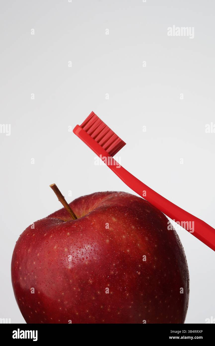 Mundhygiene mit rotem Apfel und roter Zahnbürste auf hellgrauem Hintergrund. Mundgesundheit. Stockfoto