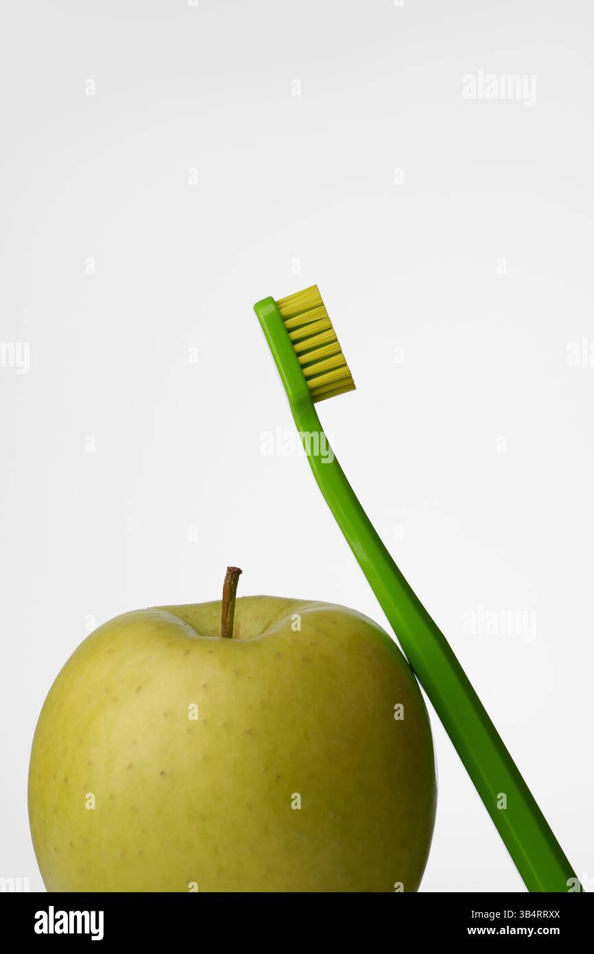 Mundhygiene mit grünem Apfel und grüner Zahnbürste auf hellgrauem Hintergrund. Mundgesundheit. Stockfoto