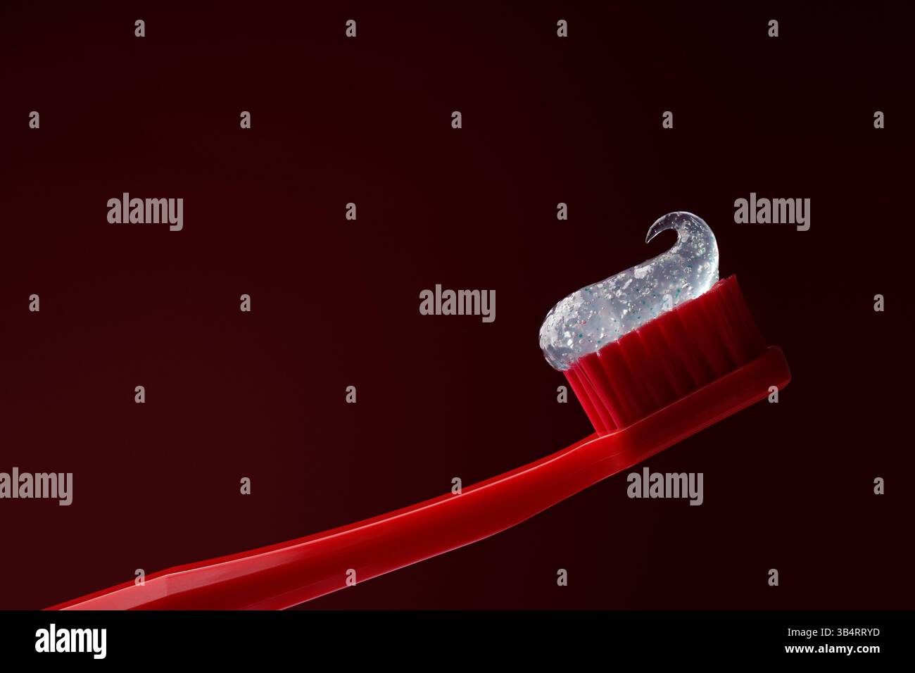 Rote Kunststoffzahnbürste mit transparenter Zahnpasta auf dunkelrotem Hintergrund. Zahnheilkunde. Stockfoto