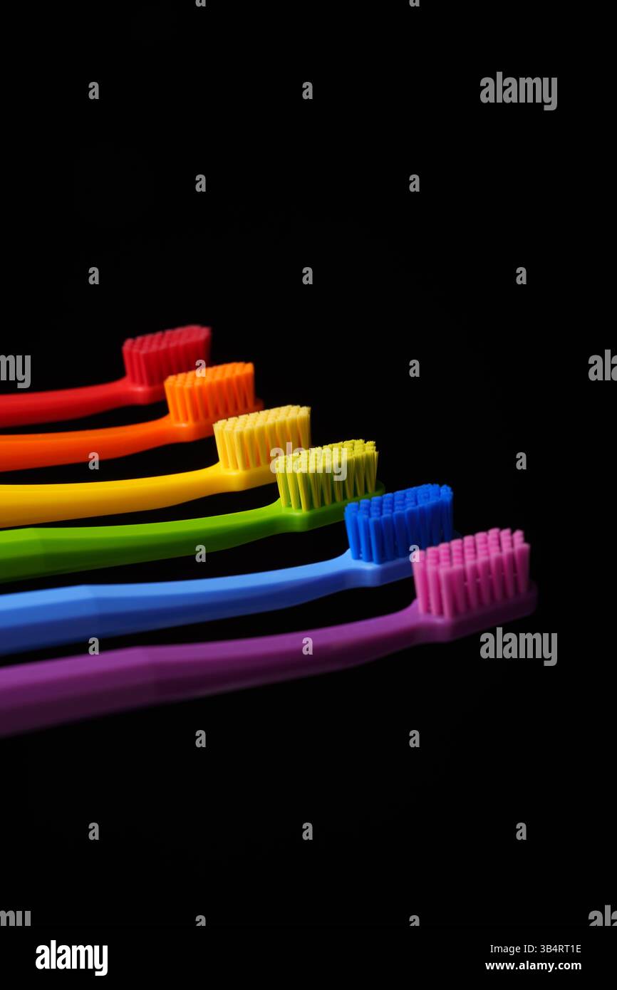 Mehrfarbige Kunststoffzahnbürsten auf schwarzem Hintergrund. Banner für die Zahnheilkunde. Farben des Regenbogens. Stockfoto