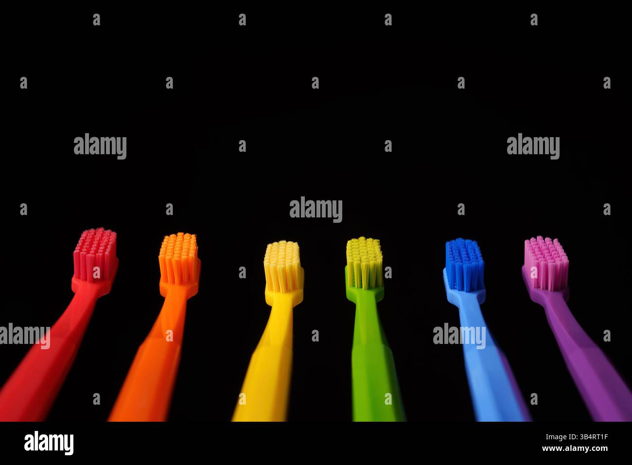 Mehrfarbige Kunststoffzahnbürsten auf schwarzem Hintergrund. Banner für die Zahnheilkunde. Farben des Regenbogens. Stockfoto