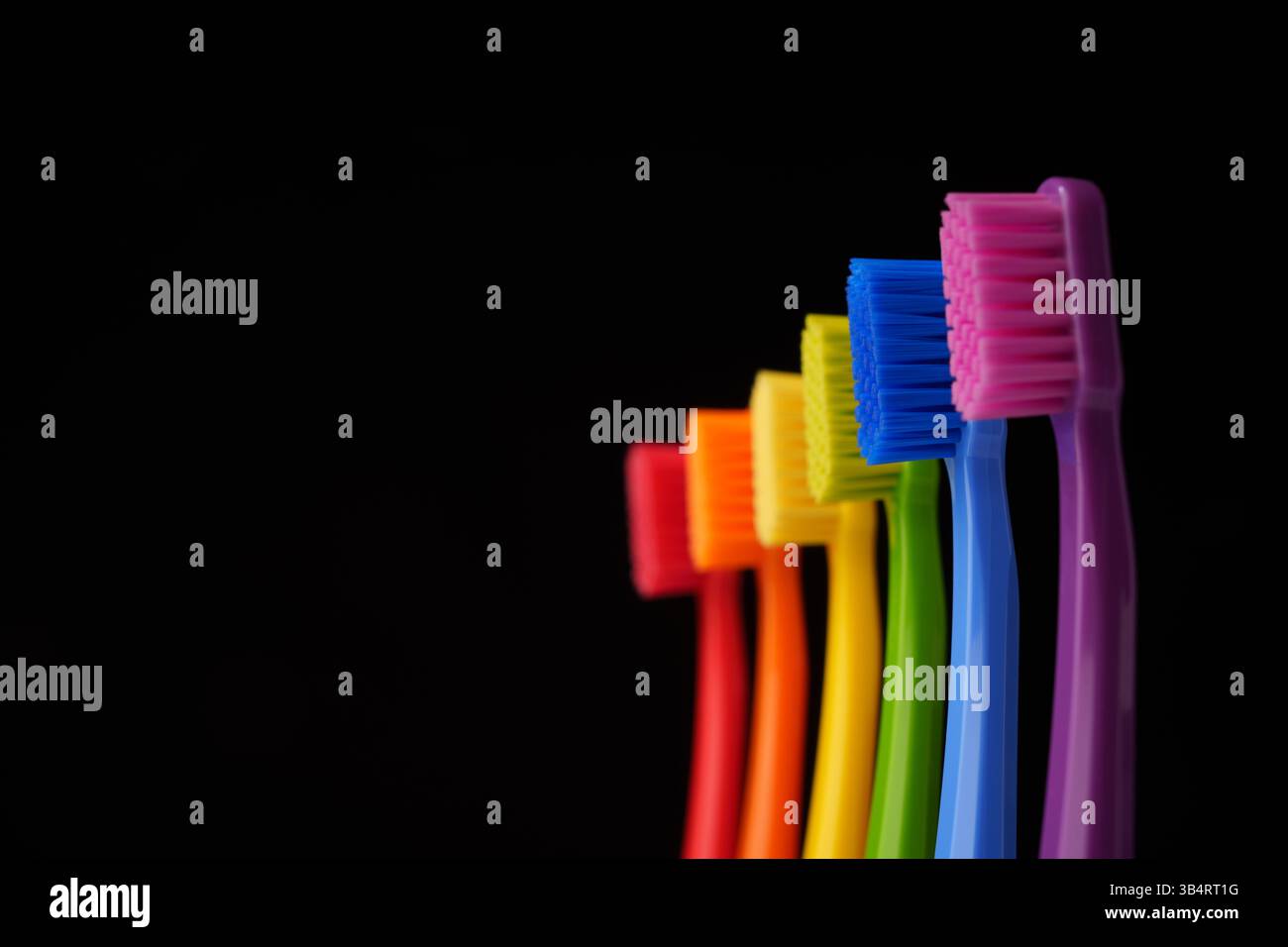 Mehrfarbige Kunststoffzahnbürsten auf schwarzem Hintergrund. Regenbogenfarben. Stockfoto